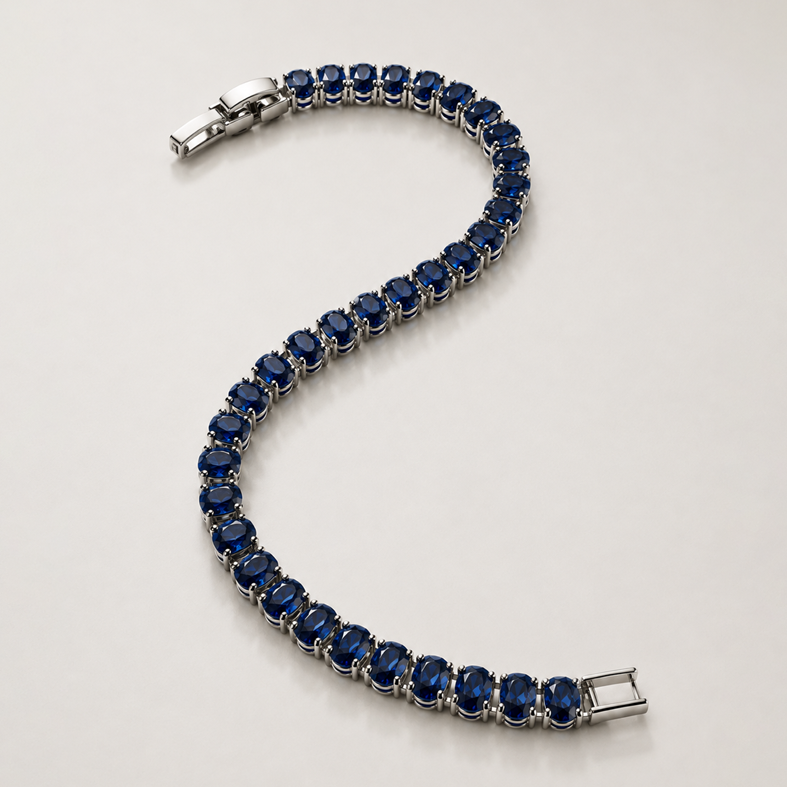 A silver tennis bracelet featuring round-cut deep blue sapphires, arranged in an S-shape on a light gray reflective surface.