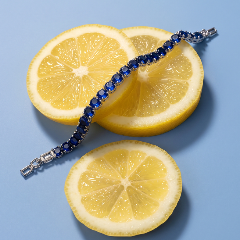 A Selforia India silver-toned bracelet with a row of deep blue gemstones, elegantly draped over three sliced yellow lemons on a solid light blue background.