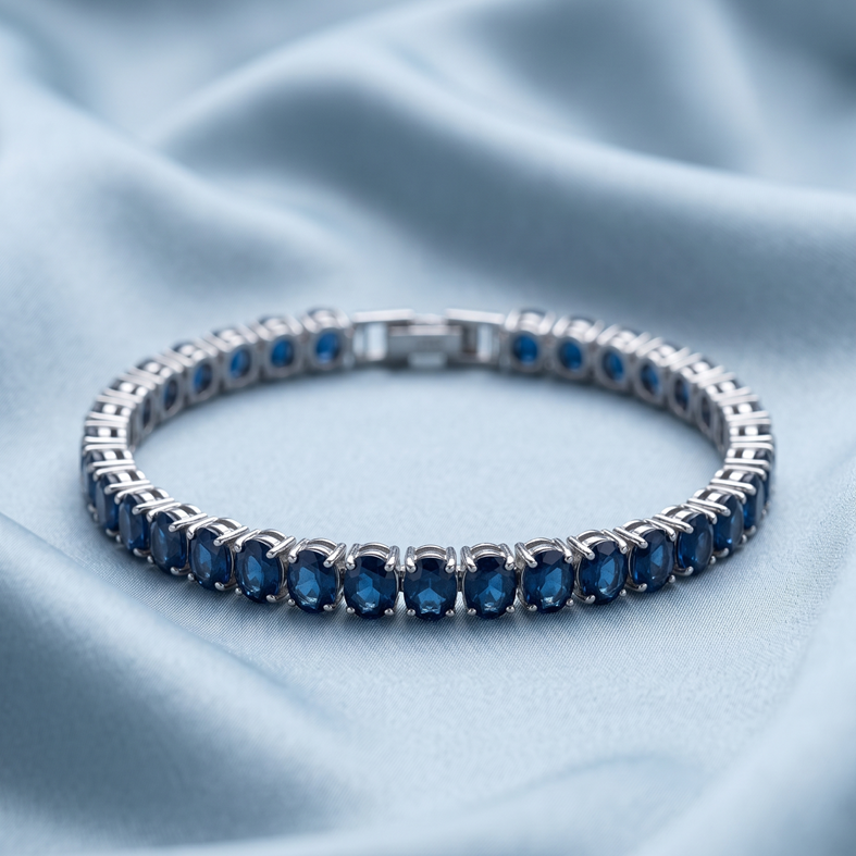A Selforia silver tennis bracelet with rectangular blue gemstones, displayed on a soft, light blue satin fabric background.
