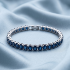 A Selforia silver tennis bracelet with rectangular blue gemstones, displayed on a soft, light blue satin fabric background.