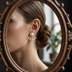 A close-up of a woman wearing a dangling pearl and gold earring, shown in profile within an ornate oval mirror with a dark wood frame.