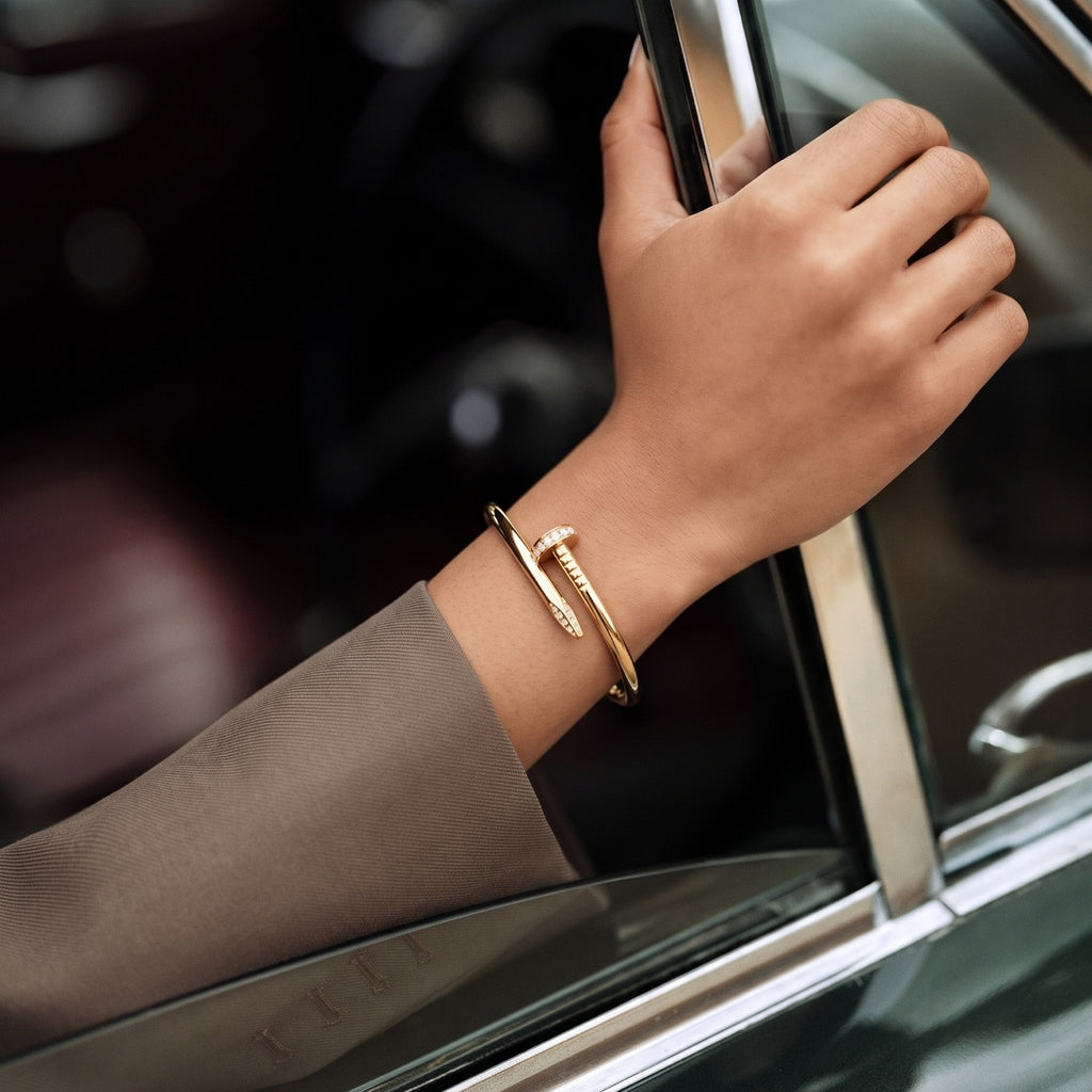A Selforia Gold-toned Nail wrap bracelet with a textured central bar, worn on a person's wrist as they lean against a car window.