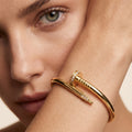 A close-up lifestyle shot of a model wearing a Selforia Gold Nail-shaped cuff bracelet with small clear stones along the top of the nail.