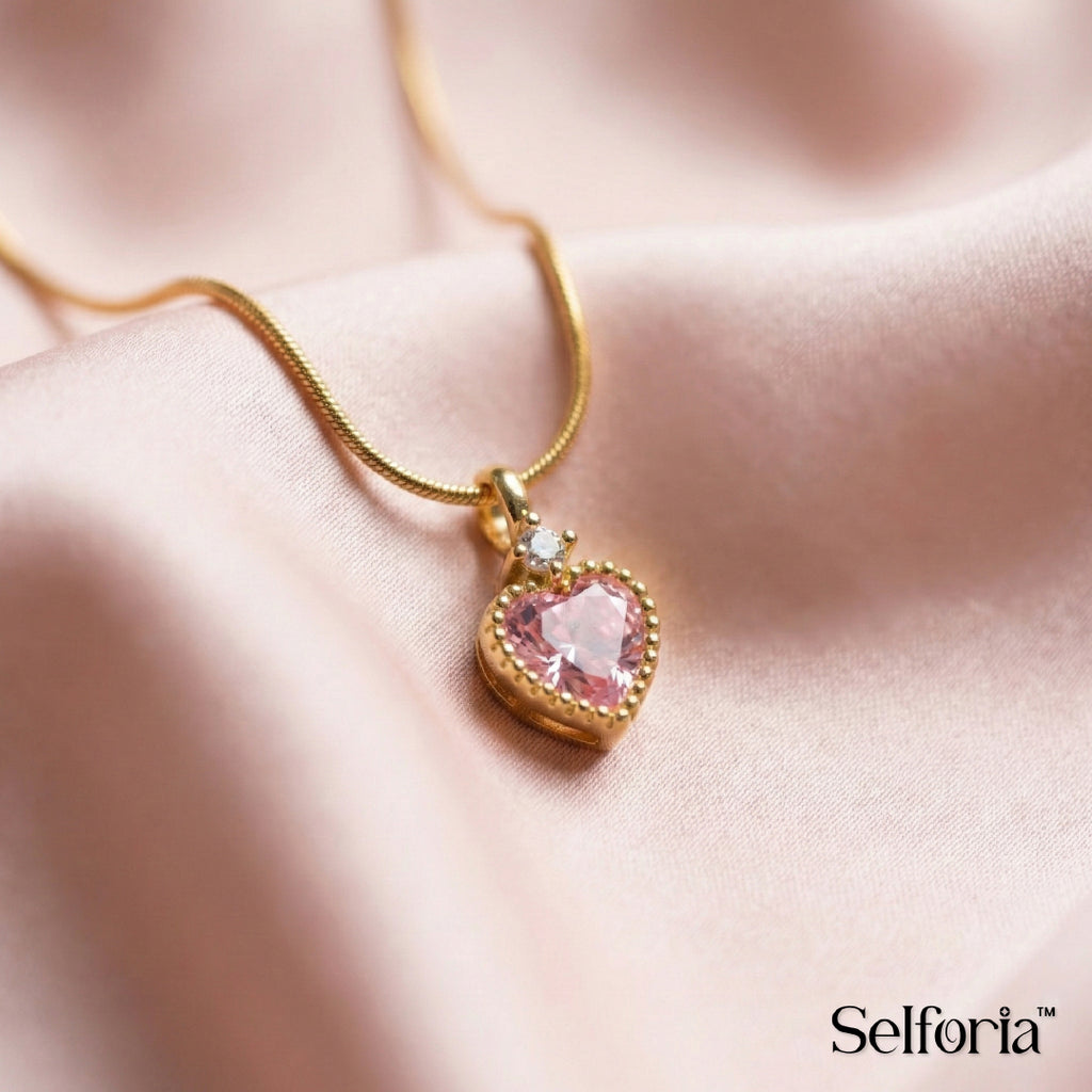 Close-up of pink heart pendant necklace featuring a polished gold setting and sparkling gemstone